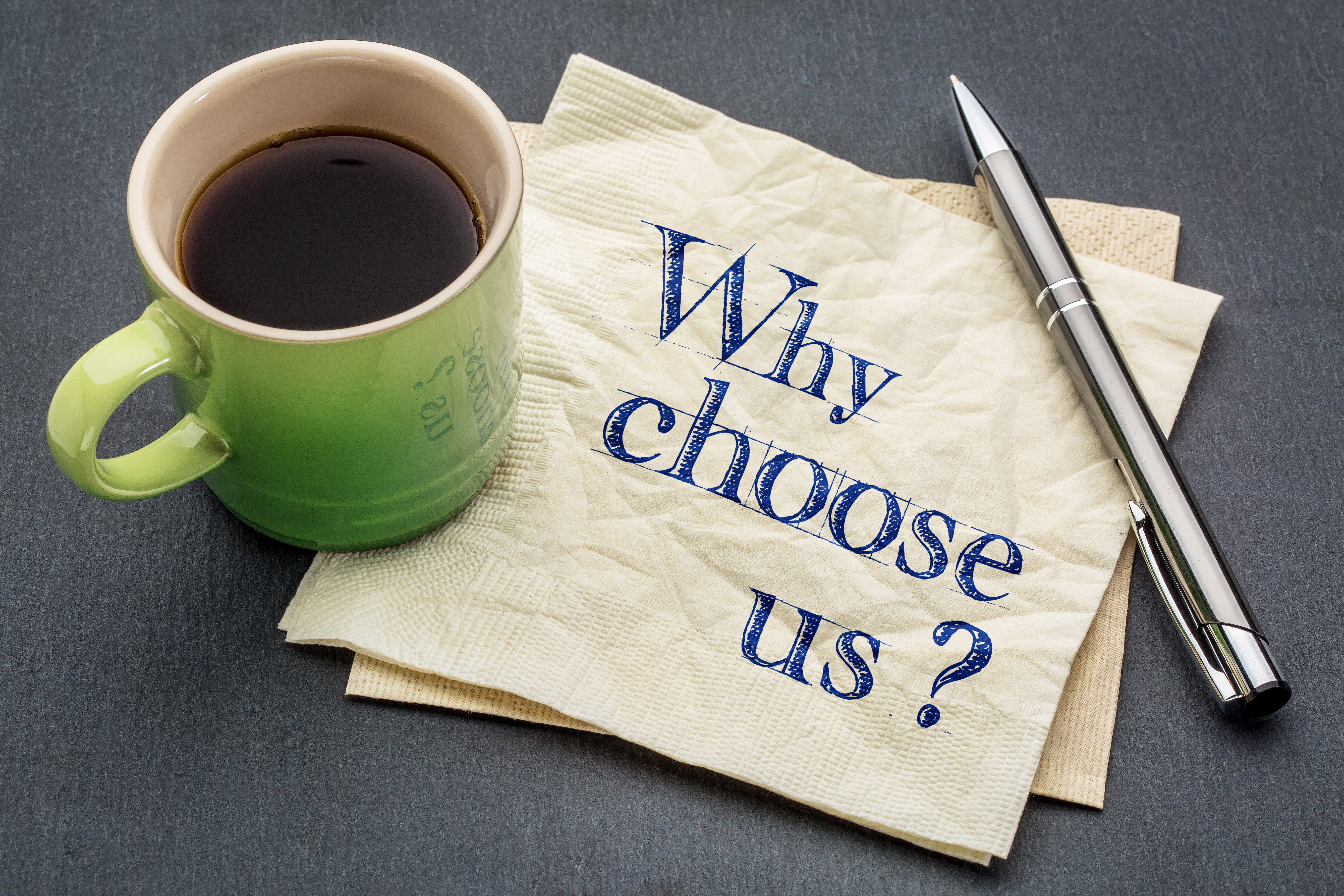 Why choose us? Handwriting on a napkin with cup of coffee against gray slate stone background